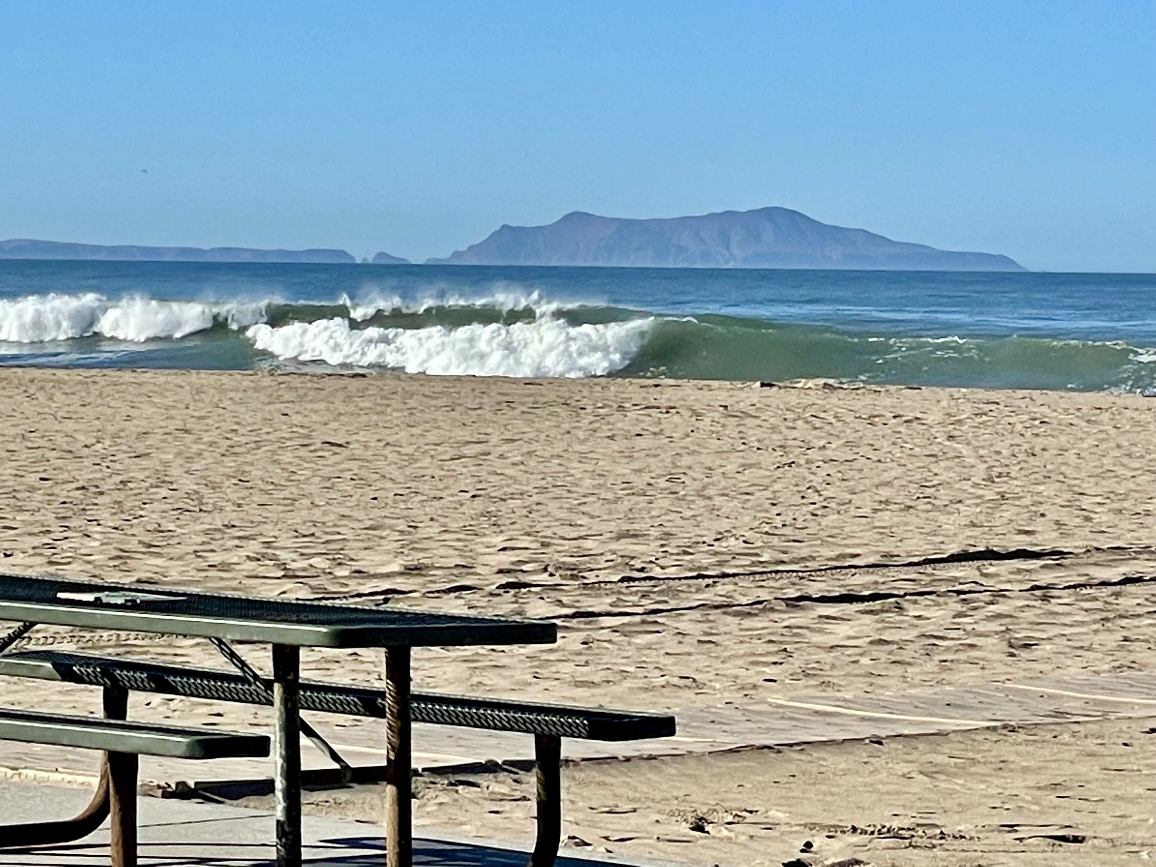 Ein Strand mit einem Holztisch und einer Aussicht auf das Meer und ferne Berge.