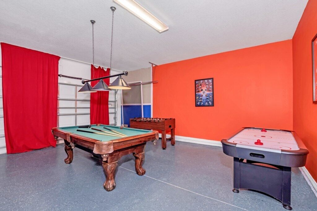A room with a pool table, foosball table, and a red curtain.