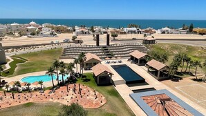 An aerial view of a resort with a swimming pool, lounge areas, and a view of the sea. - RPB Property Management (Puerto Peñasco)