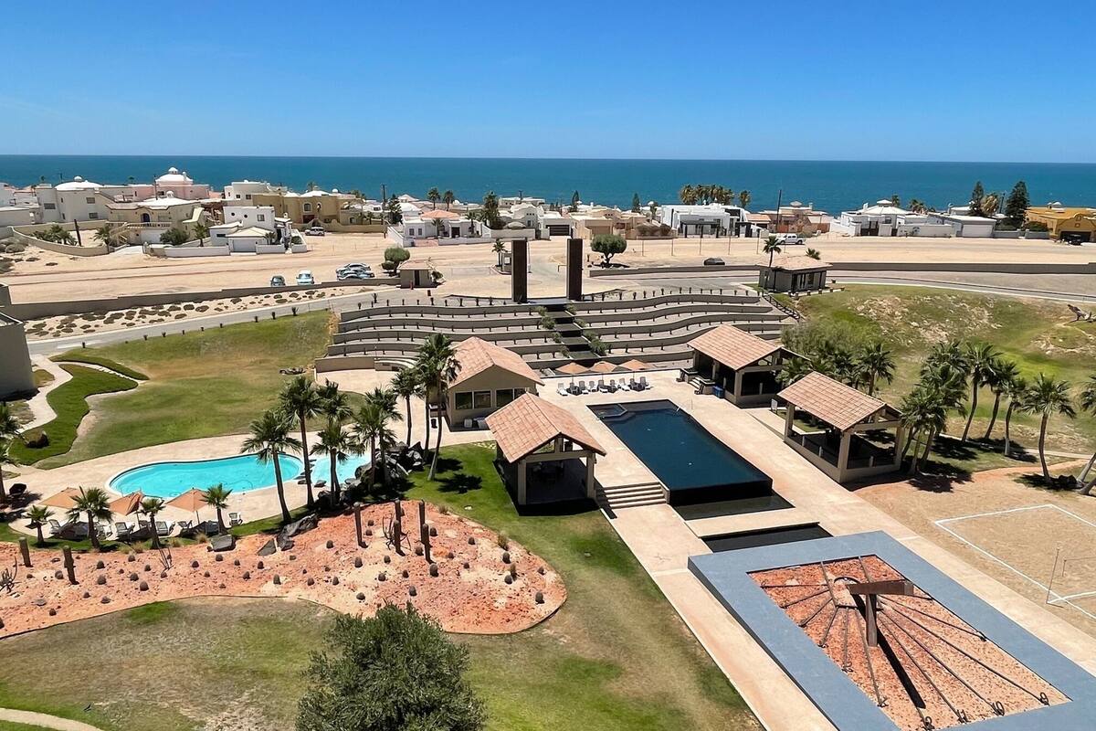 An aerial view of a resort with a swimming pool, lounge areas, and a view of the sea.