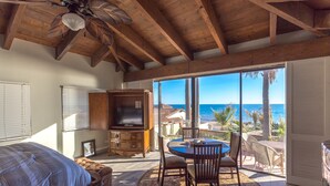 A bedroom with a bed, a wooden cabinet, a television, and a large window with a view of the ocean. - RPB Property Management (Puerto Peñasco)