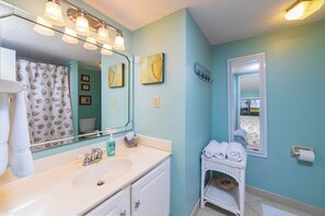 Un baño con un lavabo blanco, un espejo y una ventana con vistas a palmeras.