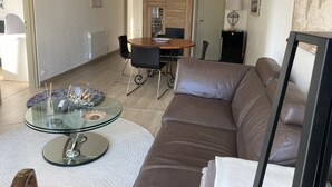 Una sala de estar moderna con una mesa de centro de vidrio, sofá de cuero y un comedor con sillas y una mesa de madera.