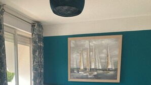 Un dormitorio con una cama grande, un cuadro de veleros en la pared y una ventana con cortinas.