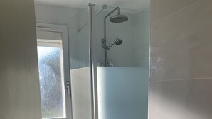 Un baño moderno con cabina de ducha de vidrio, inodoro blanco y ventana.