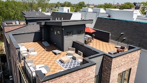 Um terraço no telhado com área de estar ao ar livre, uma mesa e um guarda-sol vermelho.