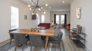 Uma sala de estar moderna com uma mesa de jantar de madeira, cadeiras estofadas cinzas, um sofá vermelho e um abajur de chão preto.