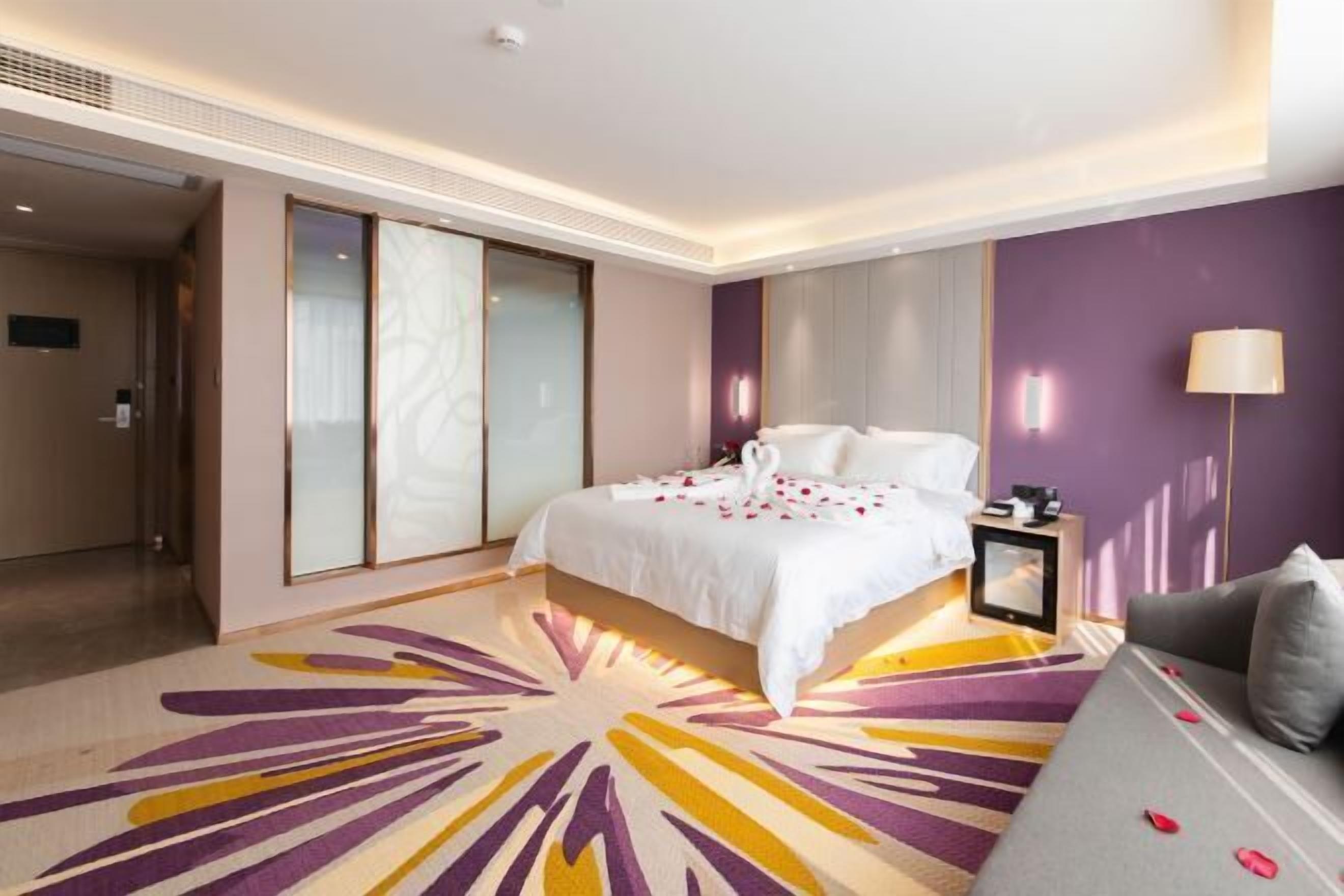 Una habitación de hotel con cama, sofá, mesita de noche y una ventana grande.