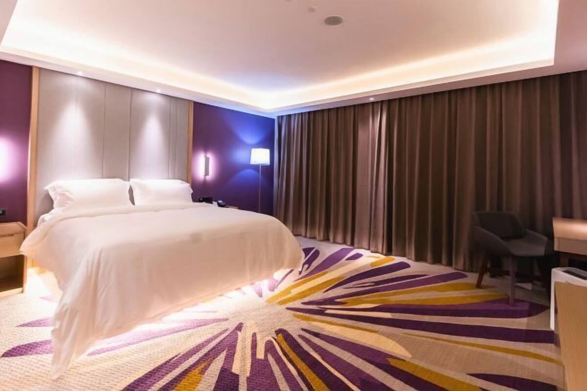 A modern hotel room with a large bed, a desk, and a chair.