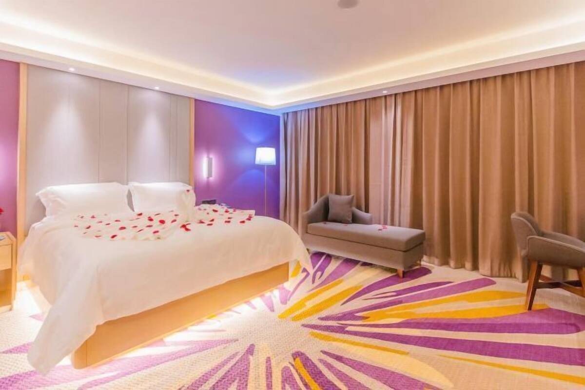 A hotel room with a bed, a sofa, a chair, and a large window with curtains.