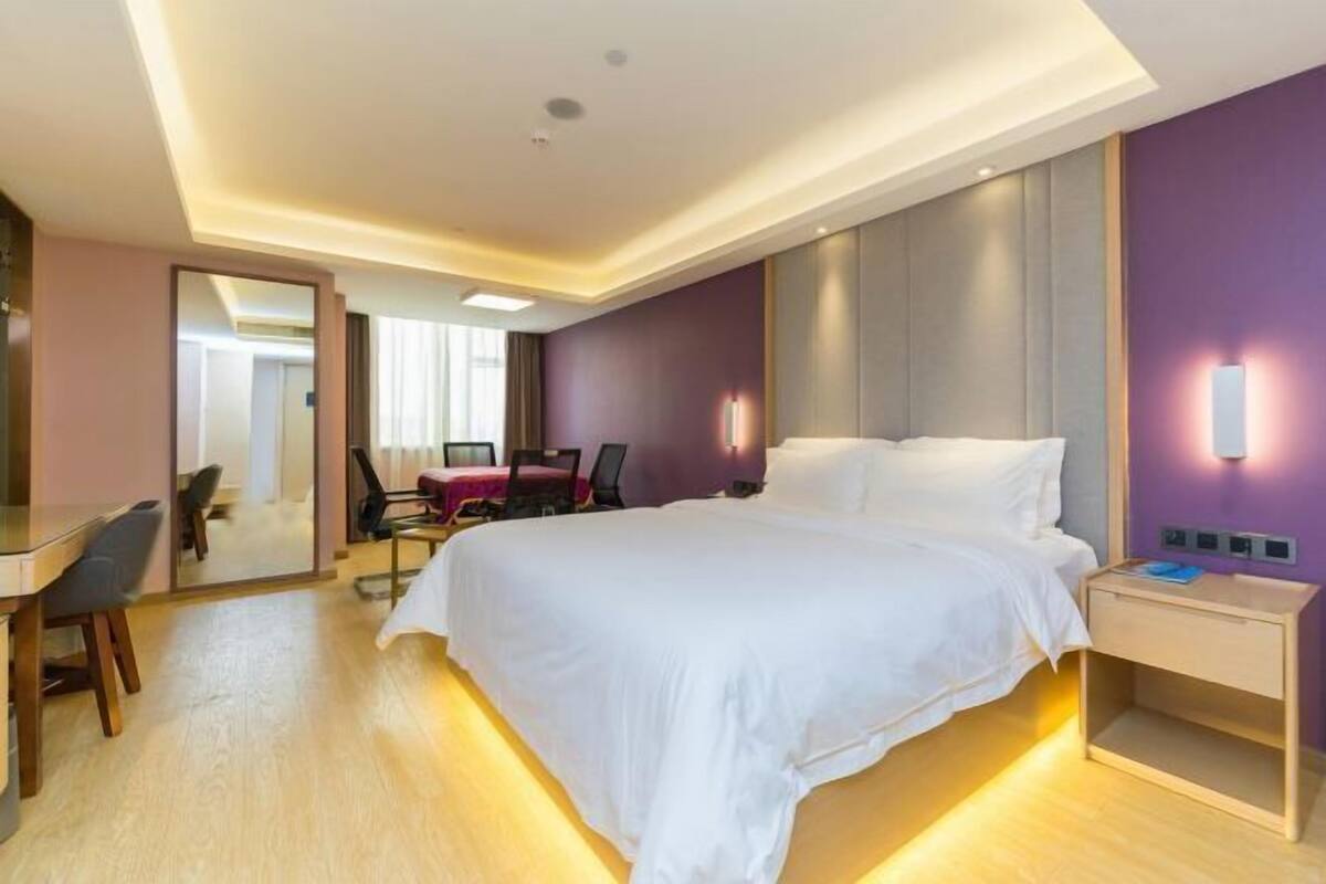 A hotel room with a large bed, a desk, a chair, and a mirror.