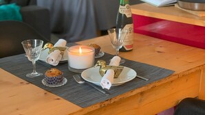 Puisesta ruokapöydästä on katettu ateria: pöydällä on kynttilä, pullo, lasi, lautanen, jossa on servetti, muffinssi ja haarukka.