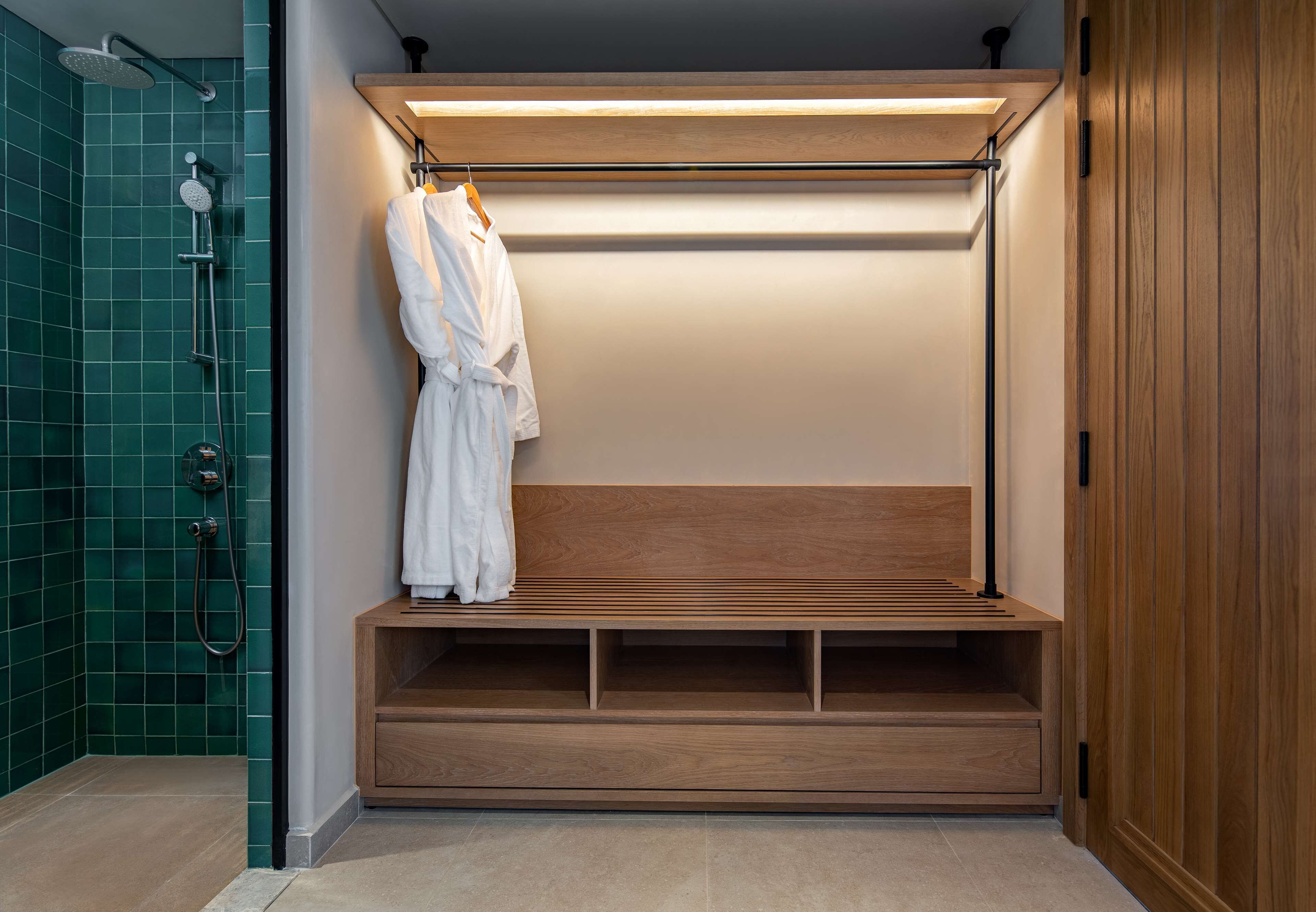 A modern bathroom with a wooden bench, a hanging robe, and a shower area.