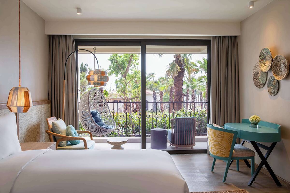 Habitación de hotel con cama, una silla colgante, una mesa y vistas al exterior.