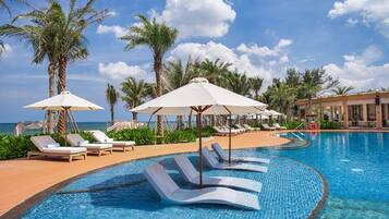 A pool area with lounge chairs and umbrellas, surrounded by palm trees and a clear sky.