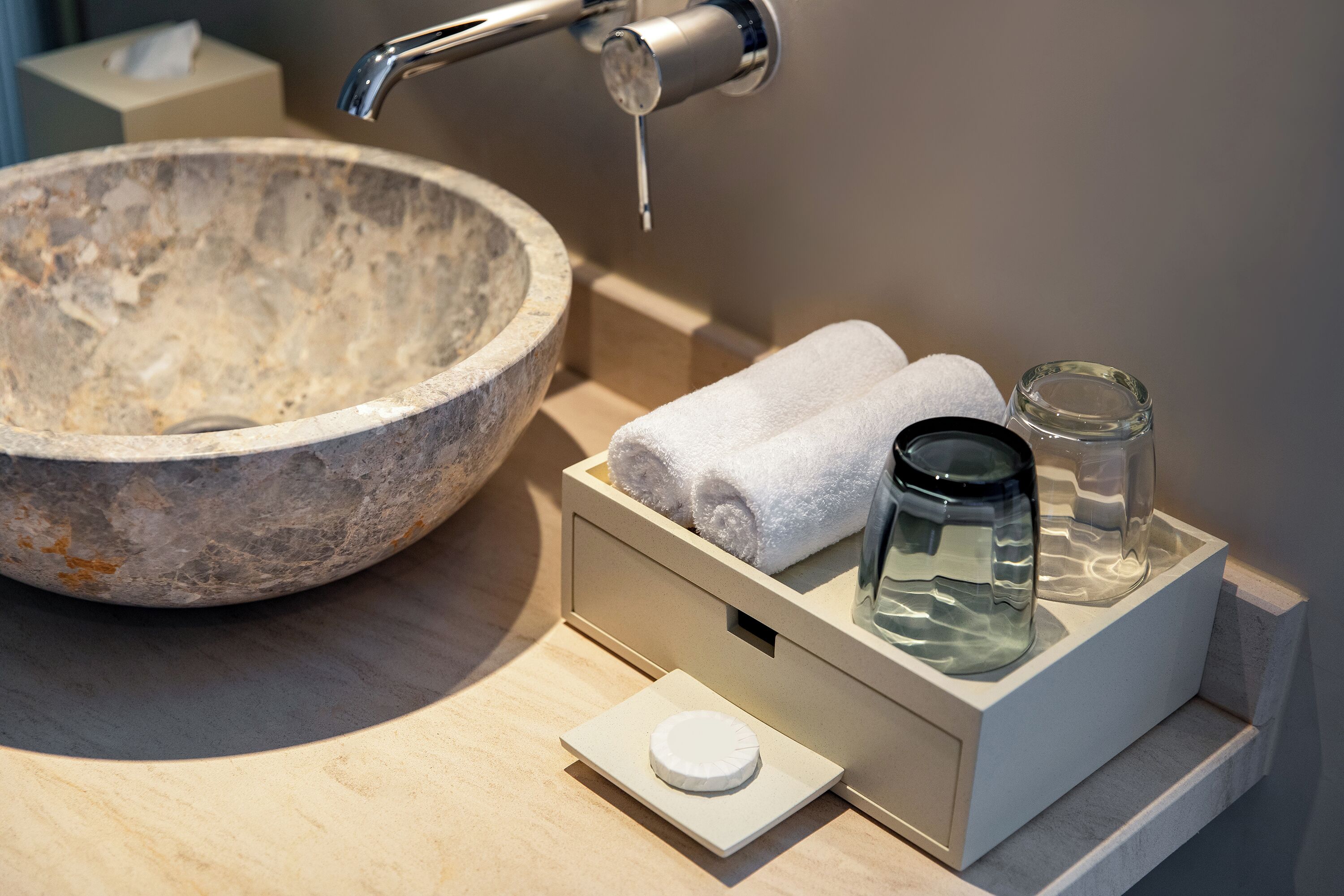 A bathroom with a stone sink, a towel warmer, and a glass jar.