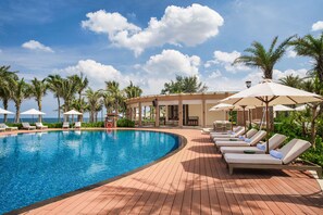 A poolside area with lounge chairs, umbrellas, and palm trees. - Radisson Resort Phan Thiet (Phan Thiet)