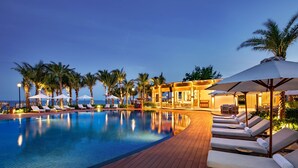 A poolside area with lounge chairs and umbrellas, palm trees, and a view of the ocean. - Radisson Resort Phan Thiet (Tien Thanh)