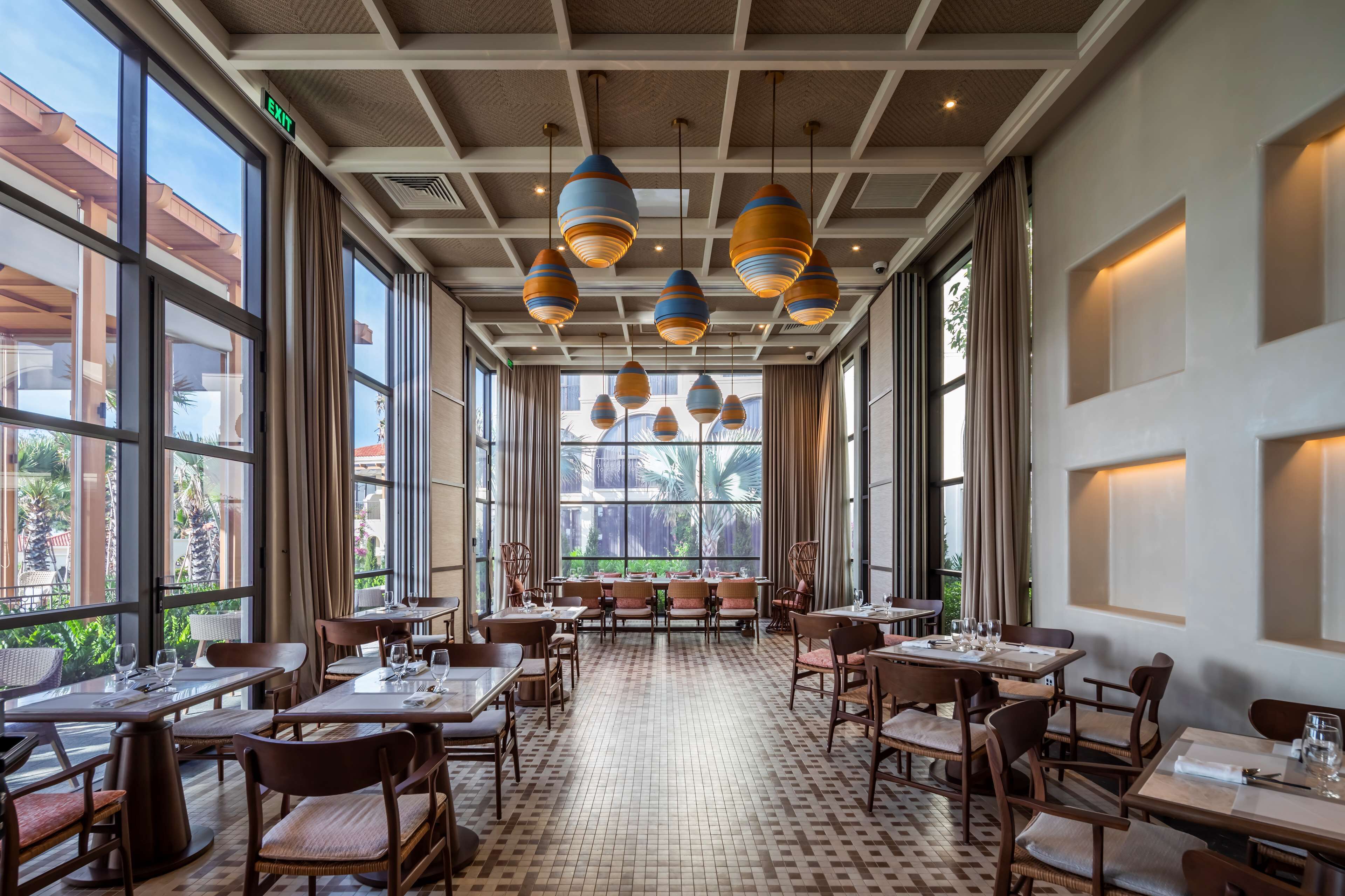 A spacious restaurant with high ceilings, large windows, and modern pendant lighting.