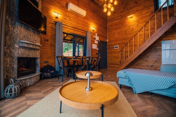 A cozy cabin interior with a fireplace, wooden floors, a dining area, and a staircase.