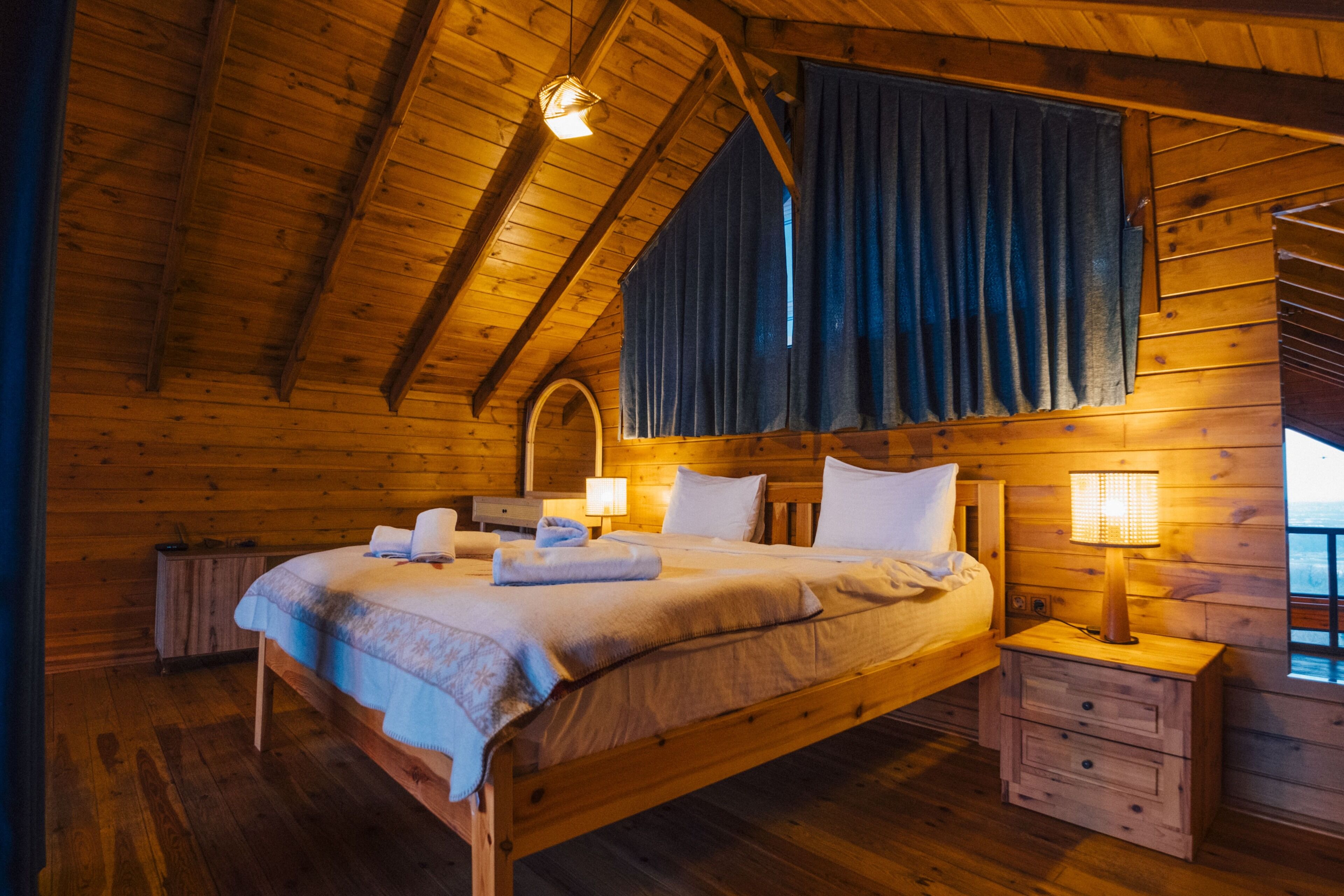 A wooden cabin bedroom with a bed, bedside tables, and a window.