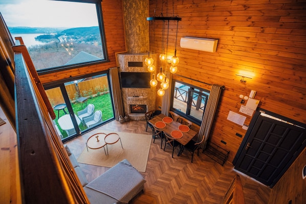 A wooden interior with a fireplace, dining area, and large windows overlooking a green landscape. - Woodlodge Country Sapanca (Sapanca)