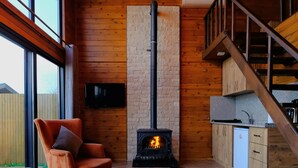 A cozy living room with a fireplace, wooden walls, a sofa, and a kitchen area with a staircase. - Woodlodge Country Sapanca (Sapanca)