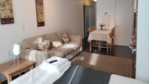 Quarto de hotel moderno com cama, sofá, mesa de jantar e pequena mesa com abajur.