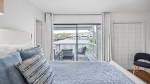 Quarto com cama, poltrona, varanda e vista para a água e edifícios.
