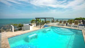 A swimming pool with a view of the ocean, lounge chairs, and a covered area with steps leading to the pool. - Sunset Gecko Condos - Unit 1A (Placencia)