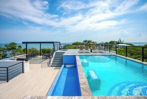 Une piscine à débordement située sur le toit, avec une terrasse en bois, des espaces de détente en plein air et une vue sur l’océan.