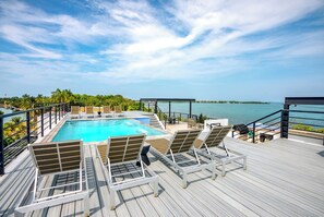 A poolside area with lounge chairs, a pool, and a view of the sea. - Sunset Gecko Condos - Unit 1A (Placencia)