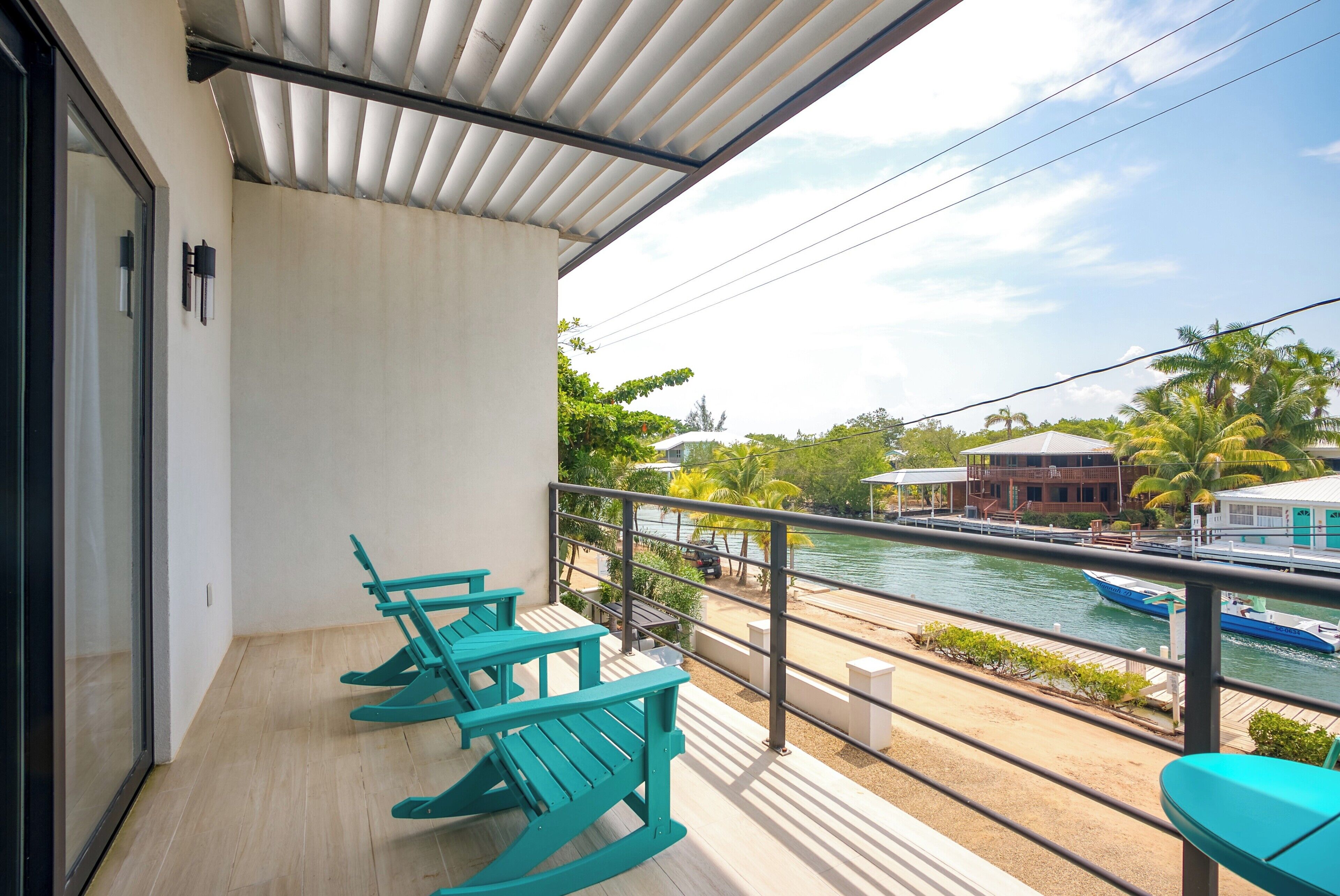 A balcony with turquoise chairs, a view of a river, and a building across the water.