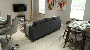 Una sala de estar moderna con un sofá gris, una mesa de comedor para cuatro personas y un televisor montado en la pared.