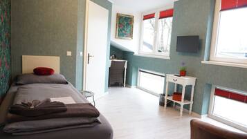 Un dormitorio con cama, una mesita, una silla, un televisor y una ventana con persianas.