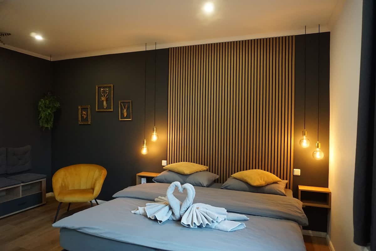 A modern hotel room with a bed, two nightstands, a yellow armchair, and a wall with vertical wooden slats.