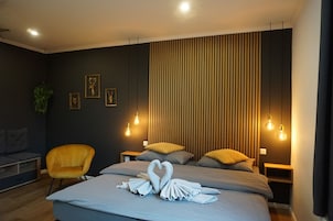 A modern hotel room with a bed, two nightstands, a yellow armchair, and a wall with vertical wooden slats.