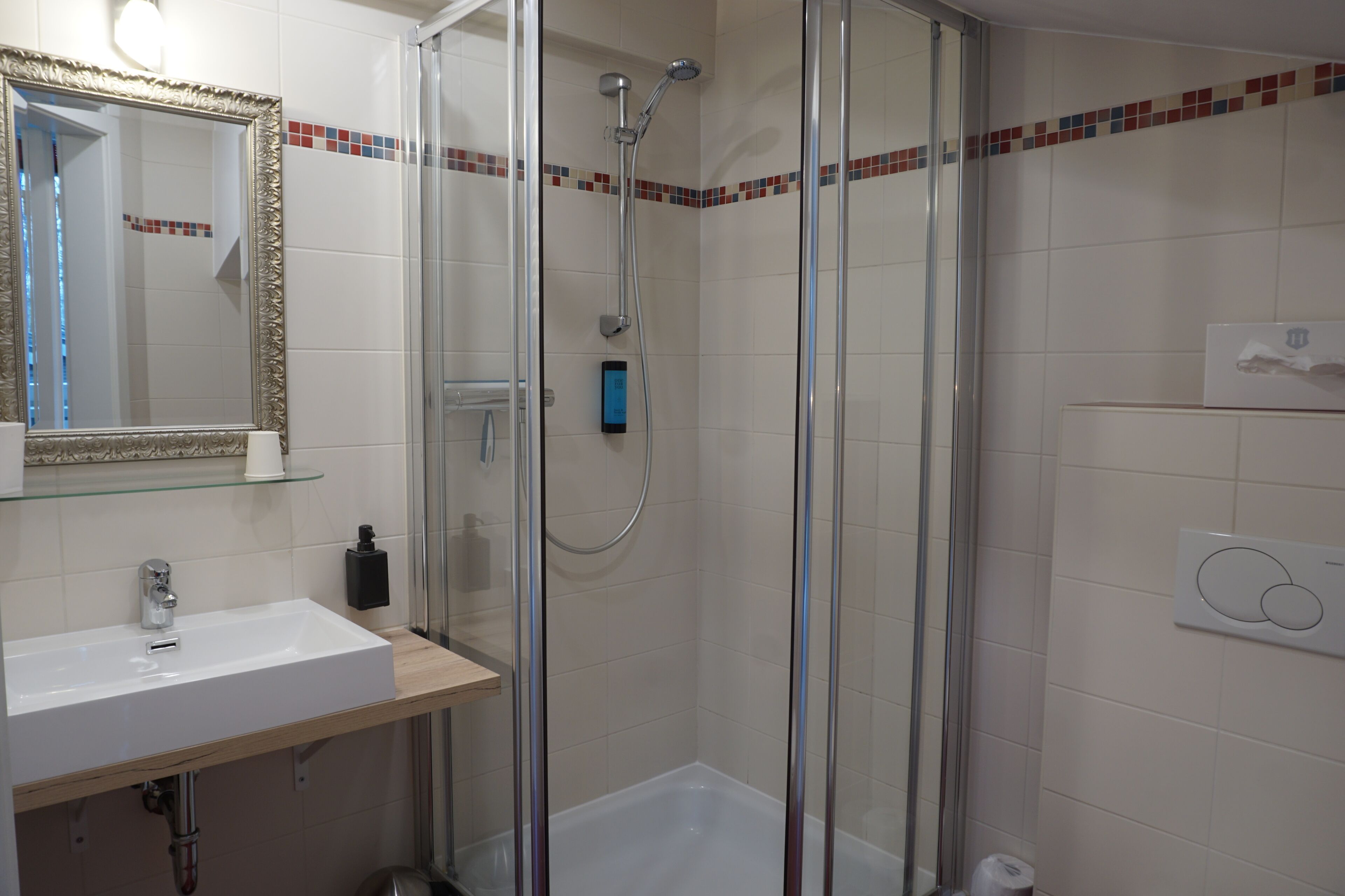 A bathroom with a glass-enclosed shower, a white sink, and a mirror with a decorative frame.