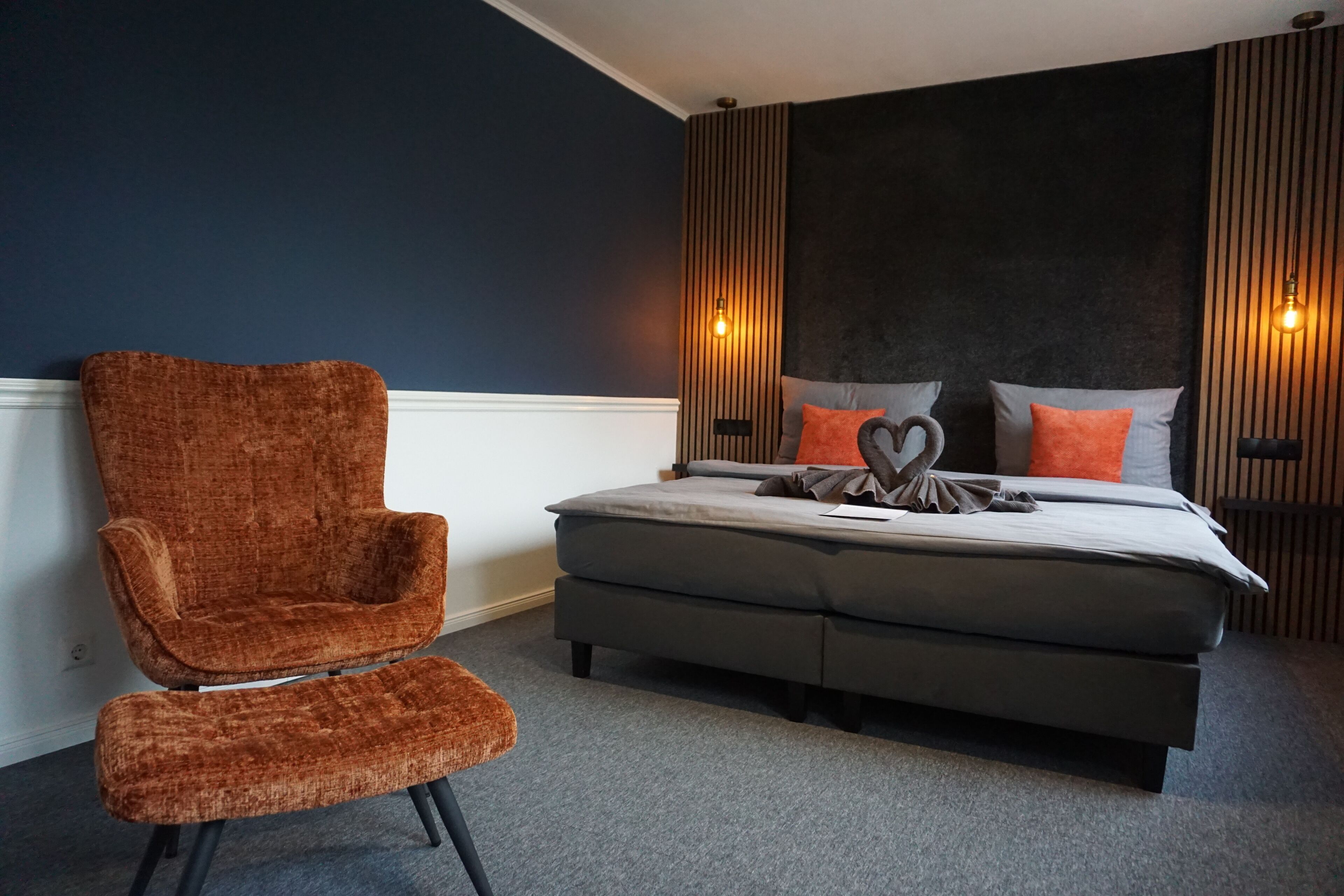A bedroom with a bed, a brown chair, and two wall-mounted lights.