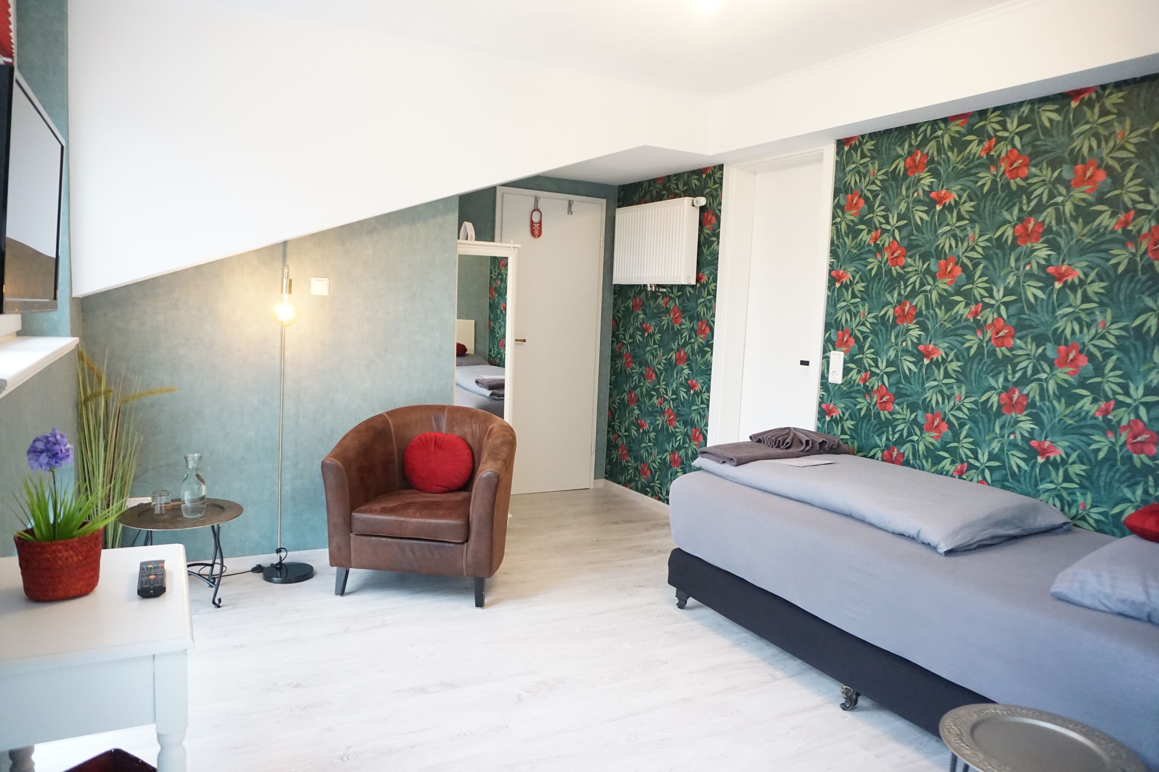 A modern bedroom with a bed, a chair, a small table with a plant, and a floor lamp.