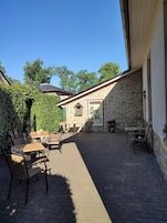 A patio area with brick flooring, outdoor seating, and a brick building with a window.
