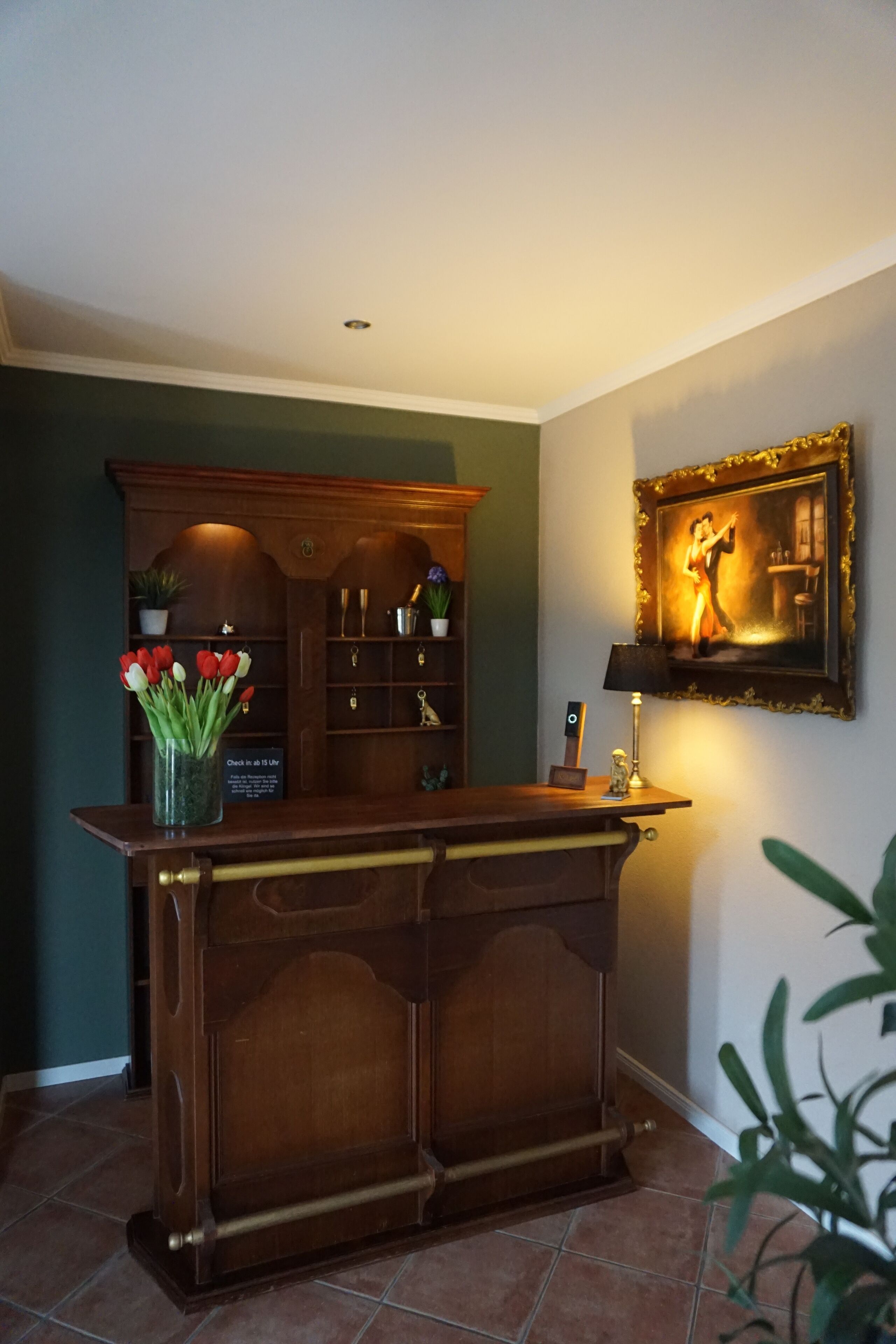 A reception desk with a vase of red and white tulips, a framed painting, and a lamp on the wall.