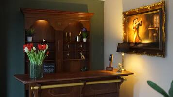 A reception desk with a vase of red and white tulips, a framed painting, and a lamp on the wall.