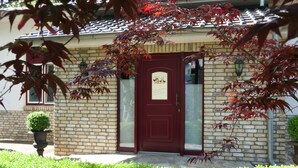 Una casa de ladrillo con puerta roja, un pequeño jardín delantero y una planta en maceta.