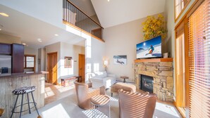 A spacious living area with a high ceiling, a stone fireplace, and a large window with blinds. - Antlers Gulch 403 (Keystone)