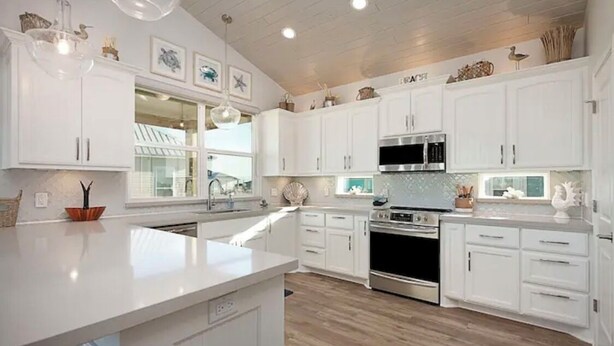 Una cucina moderna con mobili bianchi, un'isola centrale, elettrodomestici in acciaio inossidabile e decorazioni alle pareti.