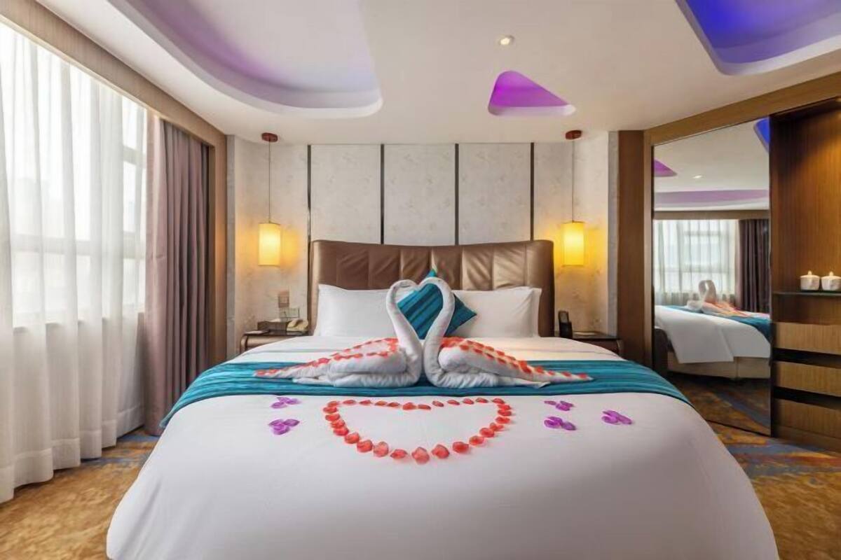 Ein Hotelzimmer mit einem großen Bett, einer herzförmigen Dekoration auf dem Bett und einem Spiegel an der Wand.