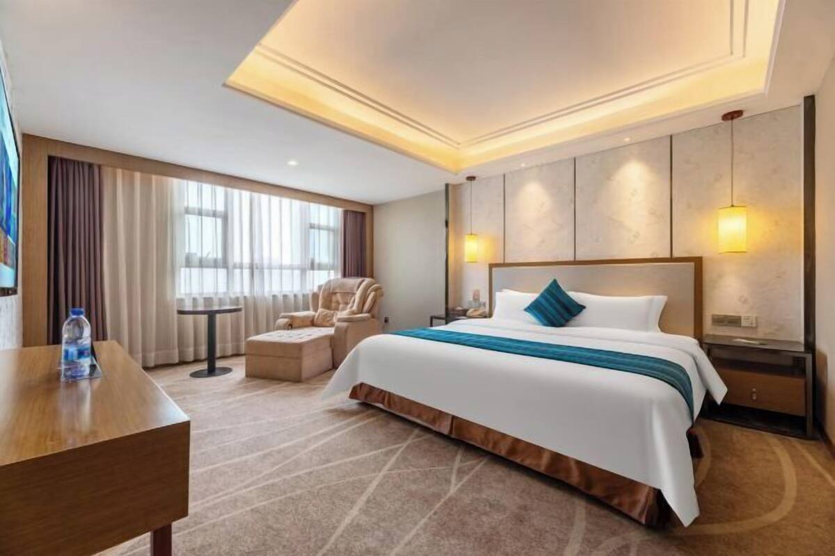 Ein Hotelzimmer mit einem großen Bett, einem Schreibtisch, einem Sessel und Blick ins Freie.
