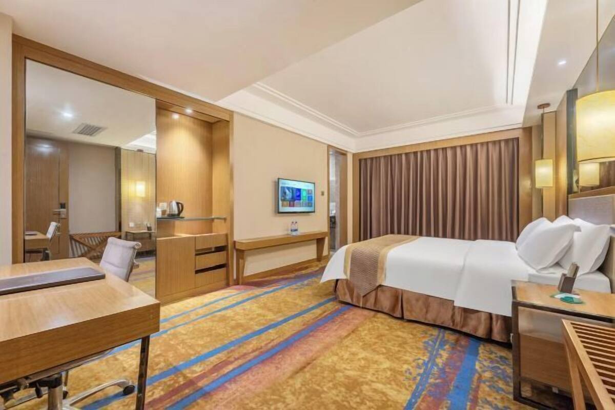 Ein Hotelzimmer mit einem Bett, einem Schreibtisch, einem Sessel, einem Fernseher und einem großen Spiegel.