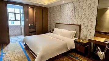 A hotel room with a large bed, a desk, a chair, a wardrobe, and a bathroom.